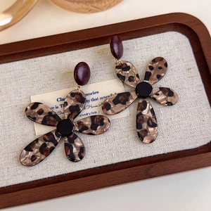 Macro view of vintage leopard print flower earrings on a minimalist jewelry display tray