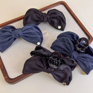Détail de pinces à cheveux à nœuds en denim et satin avec breloques dorées sur un plateau