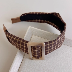 Detail of wide plaid headband in brown with a vintage resin buckle on textured tray