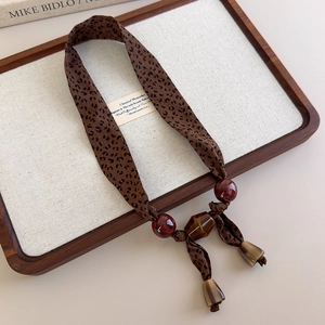 Macro shot of leopard print scarf necklace with amber beads and horn pendant on tray