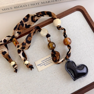 Detail of leopard print silk scarf necklace with beads and black leather heart pendant