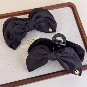 Vue détaillée de barrettes à nœuds en satin noir avec logo doré sur un plateau en bois