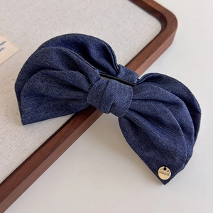 Détail d'une pince à cheveux en denim bleu avec nœud et plaque métallique dorée