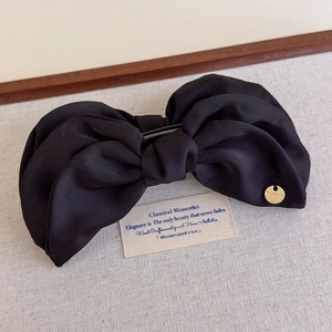 Détail d'une pince à cheveux à nœud en tissu noir avec emblème en métal doré