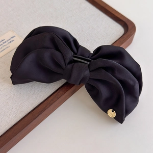Détail de la pince à cheveux noeud en satin noir avec un pendentif en métal doré élégant