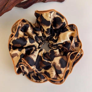 Detail of leopard print scrunchie showing glossy satin texture and orange stitched edges