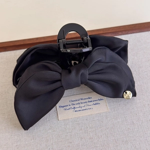 Gros plan d'une pince à cheveux avec nœud en satin noir et plaque dorée élégante