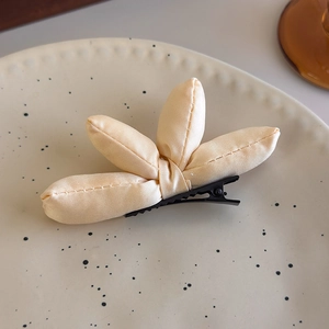 Detailed close-up of cream padded fabric bow hair clip on a minimalist ceramic plate