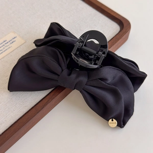 Détail d'une pince à cheveux élégante avec nœud en satin noir et logo doré brillant
