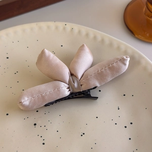 Detailed close-up of champagne satin bow hair clip with 3D padded texture and metal base