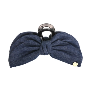 Détail de la pince à cheveux noeud en denim bleu foncé avec emblème doré de marque
