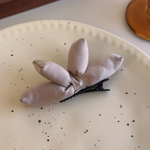 Detail of a beige padded fabric clover hair clip on a ceramic tray with a soft aesthetic