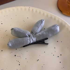 Detailed close-up of a blue padded satin bow hair clip with a black metal alligator grip