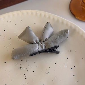Detail of grey satin padded bow hair clip with black duckbill clasp on a ceramic plate