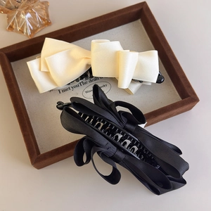 Detail of vintage satin bow banana hair clips in cream and black on a wooden tray