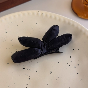 Detail of a black padded bow hair clip made of satin fabric with a metal duckbill base