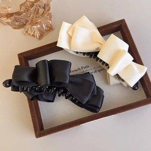 Detail of vintage satin bow banana clips in black and beige displayed in a wooden tray