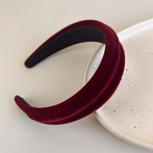 Detail of burgundy velvet padded headband resting on a cream ceramic plate with soft lighting