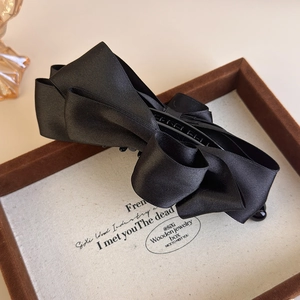 Detailed close-up of a premium black satin ribbon bow banana hair clip on a wooden tray
