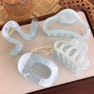 Set of four blue marble hair claws in various geometric shapes on a rustic tray