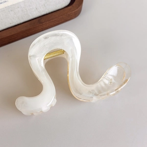 Détail macro d'une pince à cheveux ondulée blanc crème marbré avec ressort doré