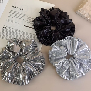 Détail de trois chouchous métalliques en noir et argent sur un fond minimaliste élégant