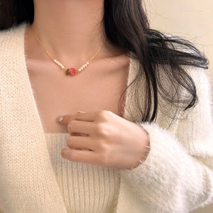 Detail of a gold rose necklace with red flower and pearls on a female model