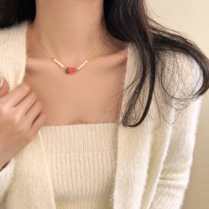 Close-up of a pink rose pendant necklace with white beads and a delicate gold chain
