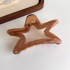 Star-shaped translucent amber claw clip with golden metal spring on white surface