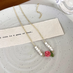 Detail of rose necklace with gold chain, white beads, and delicate enamel leaf charm