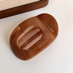 Detail of coffee amber large hair claw clip in translucent acetate on a wooden tray