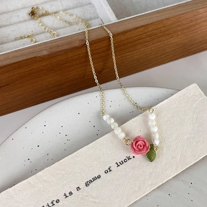 Detail shot of the beaded gold necklace featuring a 3D pink rose and white pearl pendant