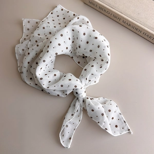 Close-up of lightweight brown polka dot scarf tied elegantly on a neutral surface