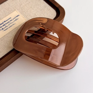 Macro shot of a glossy jelly brown hair claw clip on a linen and wood display tray
