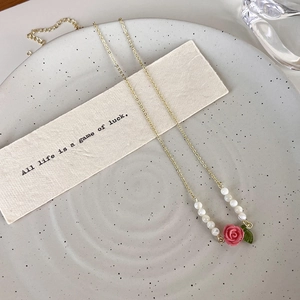 Detailed macro view of pink rose pendant necklace with white beads and golden chain