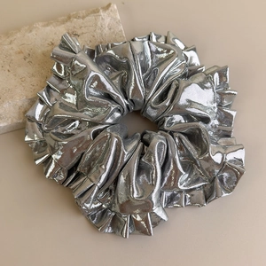 Détail d'un chouchou argenté métallisé avec texture plissée sur un fond en pierre