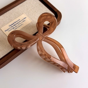 Detailed close-up of a translucent amber resin bow hair claw clip on a linen texture