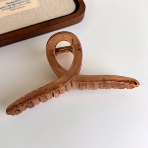 Detail of amber translucent hair claw clip with cross spiral design on minimalist background