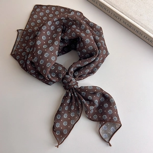 Detail of a brown floral polka dot silk scarf tied on a minimalist light background