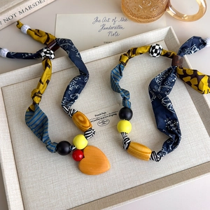 Artistic fabric patchwork necklaces with wooden beads and orange heart pendant on tray