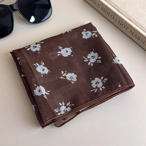 Detail view of a dark brown floral square scarf with a blue flower pattern on a book