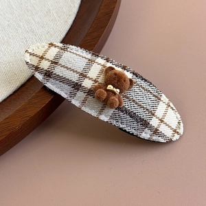 Detailed close-up of a brown flocked bear on a plaid fabric oval hair clip