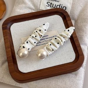 Detail of cream polka dot fabric hair clips with pearls displayed on a wooden tray