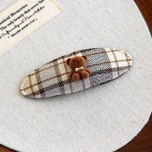 Close-up of oval plaid hair clip featuring a cute flocked bear with a golden bow