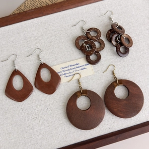 Drei Paar Vintage-Boho-Ohrringe aus Holz in geometrischen Formen auf beigem Leinenstoff