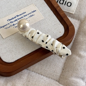 Close-up of polka dot fabric hair clip with a large cream pearl on linen background