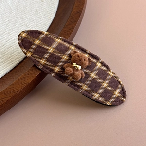 Close-up of a brown plaid fabric hair clip with a 3D plush bear and gold bow detail