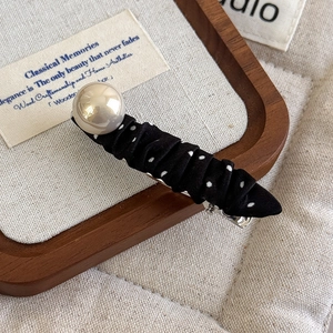 Detail of vintage polka dot fabric hair clip with a large glossy pearl on wooden tray