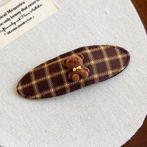 Detailed macro view of the textured brown plaid fabric and the cute plush bear on hair clip