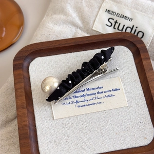 Close-up of black polka dot fabric hair clip with a large white pearl on a wooden tray